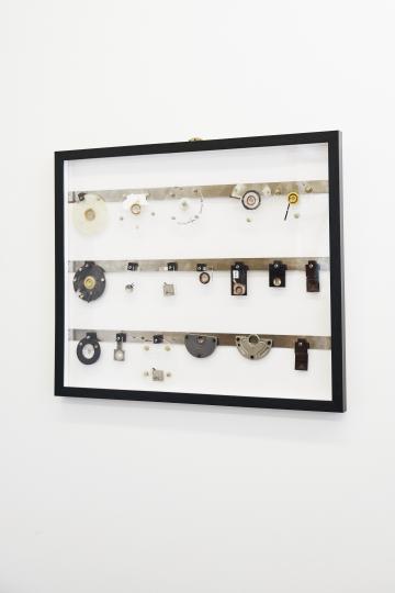 Framed display case with vintage mechanical components on a white wall.